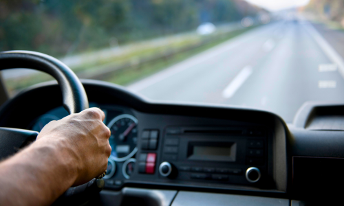 A close-up of hands on a steering wheel of a vehicle driving down the highway.